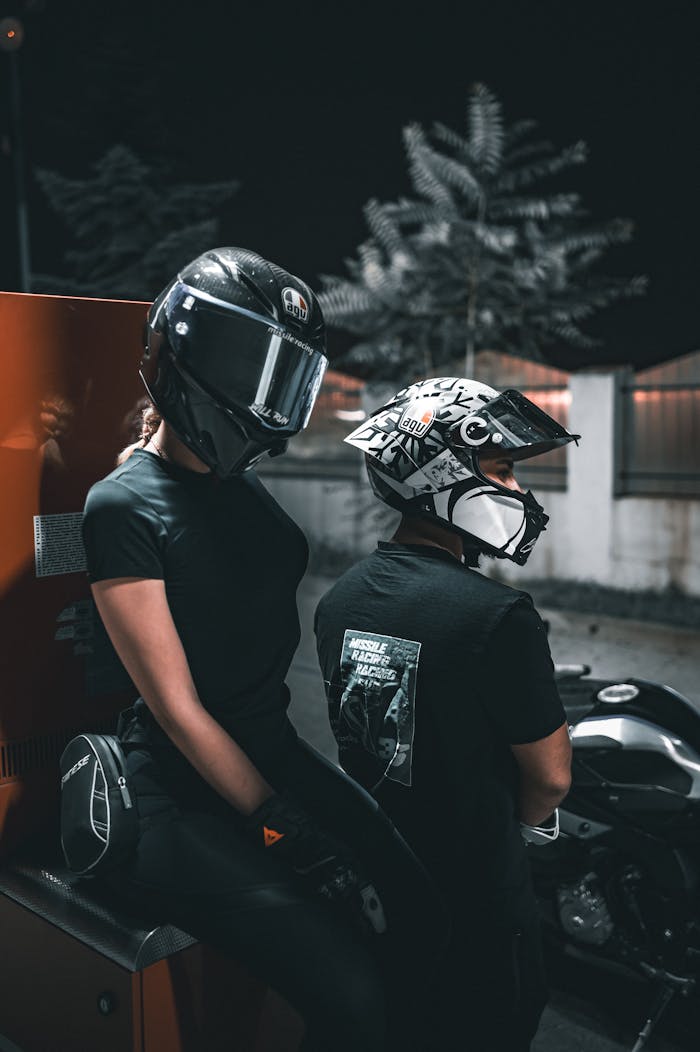 Two individuals with helmets ride motorcycles at night in an urban area.